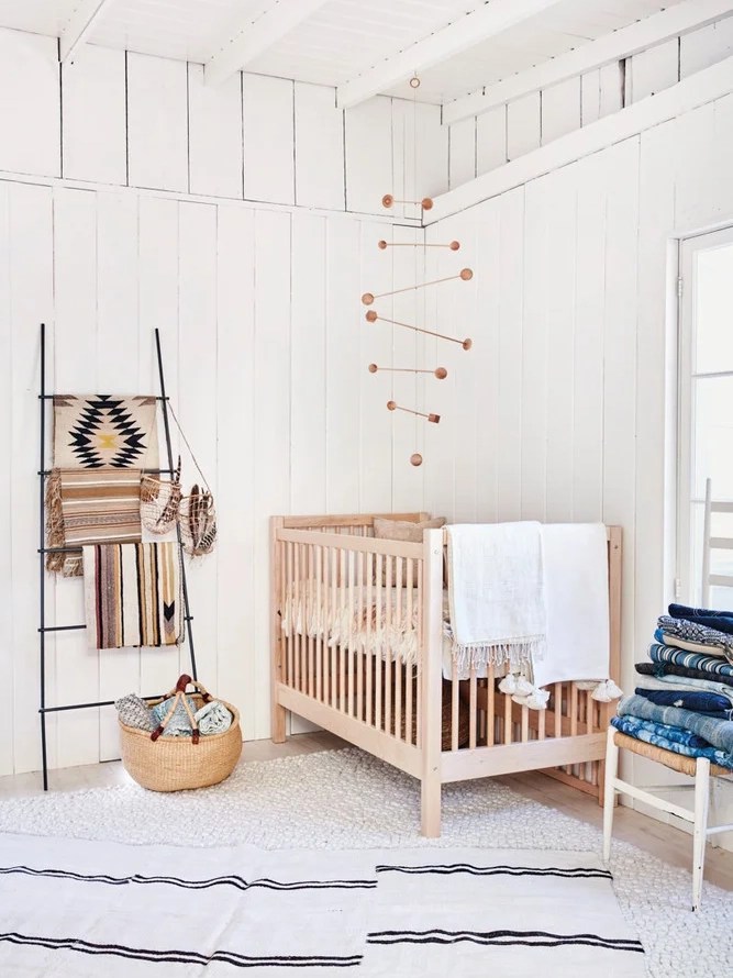 White nursery with textiles hanging on ladder and wooden mobile. 