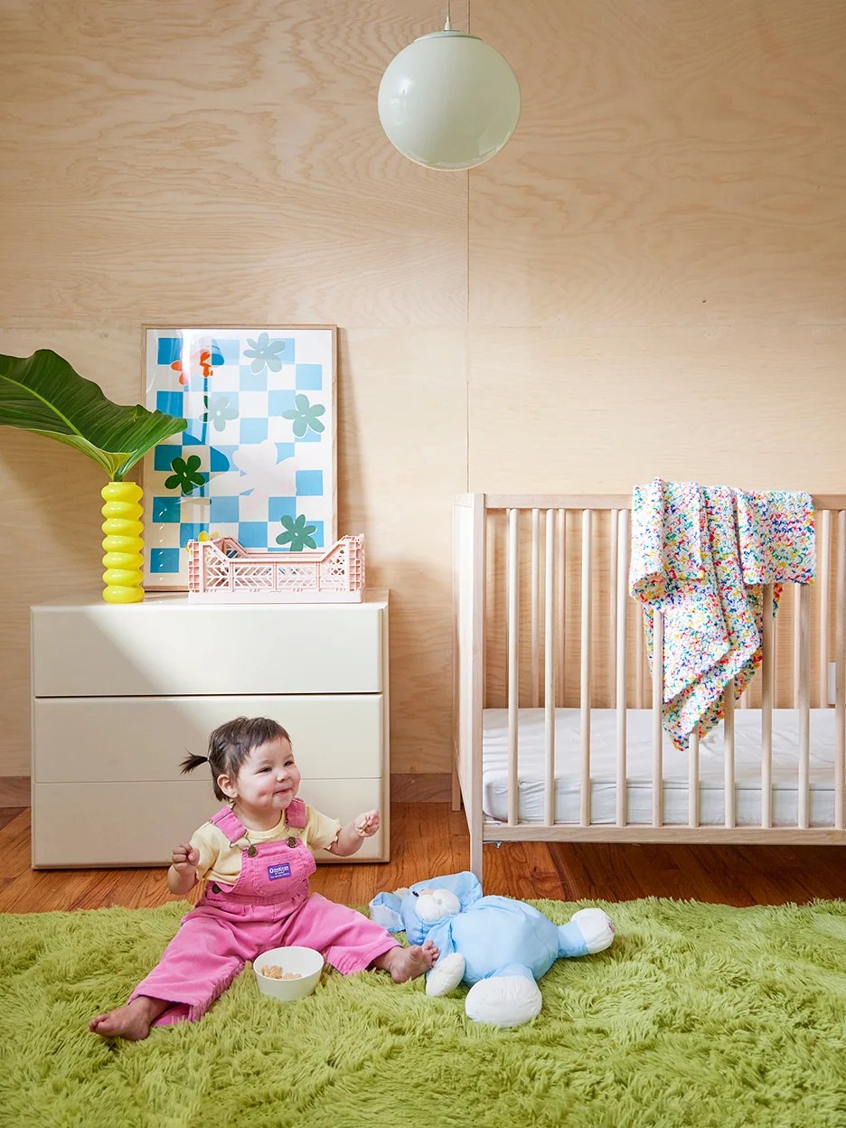 Nursery with birch plywood back wall and green fuzzy rug. 