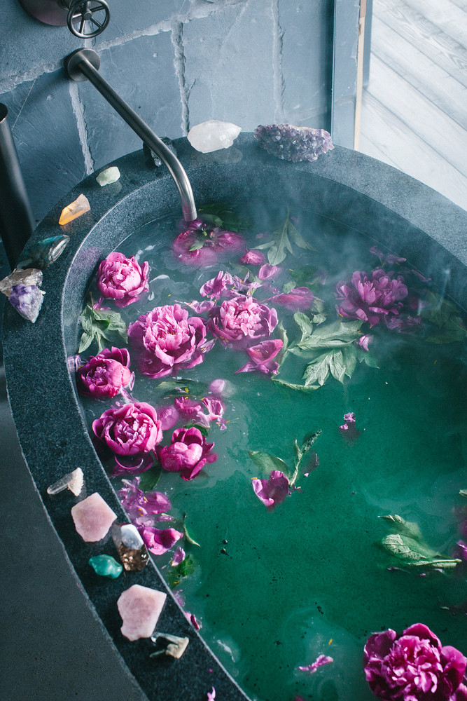 freestanding tub filled with water and flowers and lined with crystals