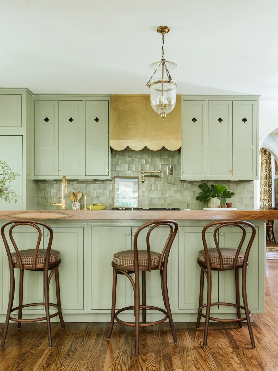 Sage green kitchen cabinets with brass scalloped hood.