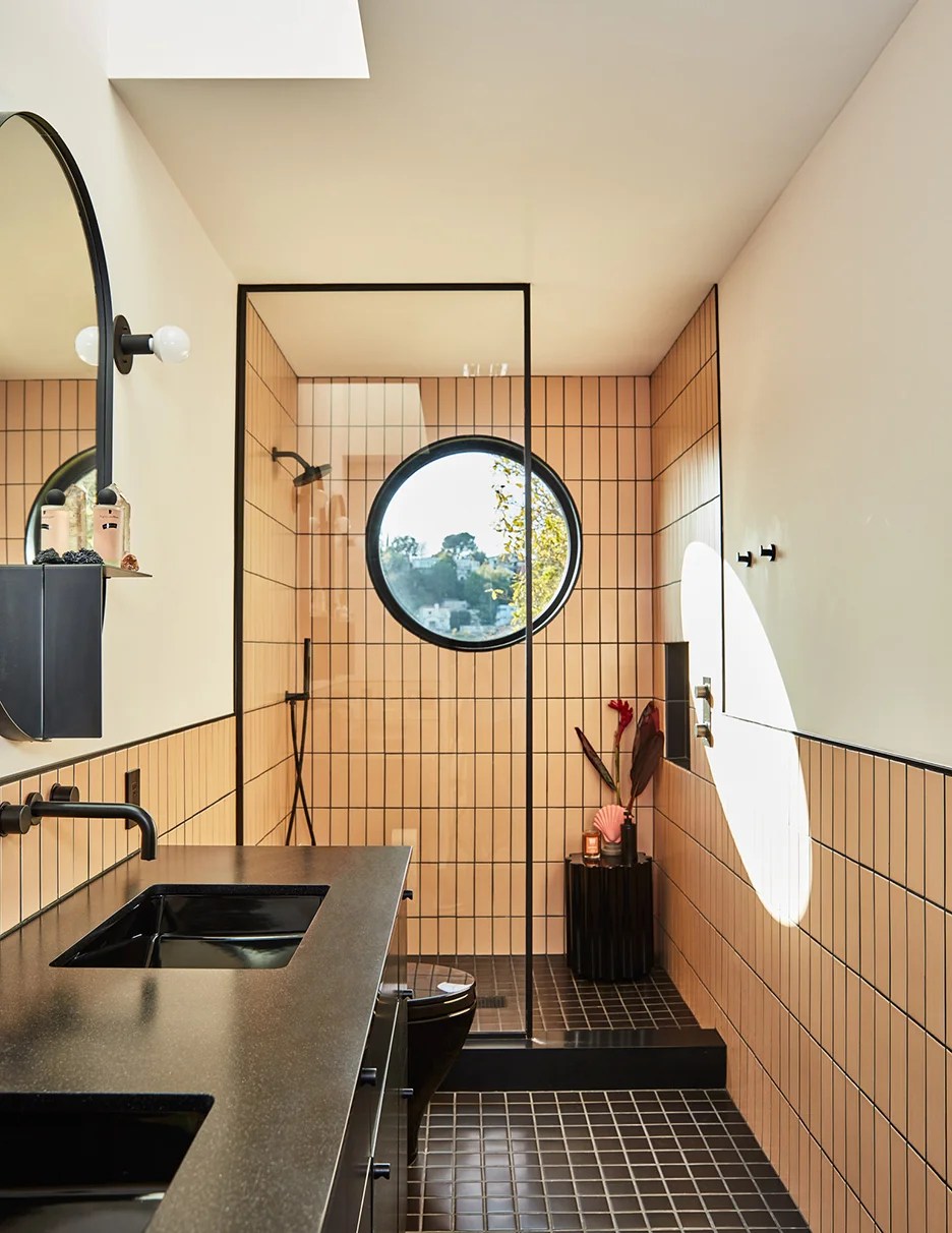 Apricot-hue tiled bathroom with black floors and round window.