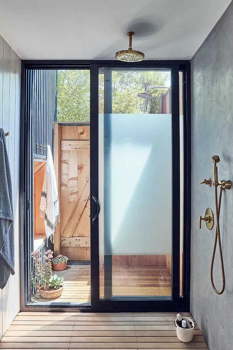 Blue plaster-style shower with black framed doors that open to outdoor shower.