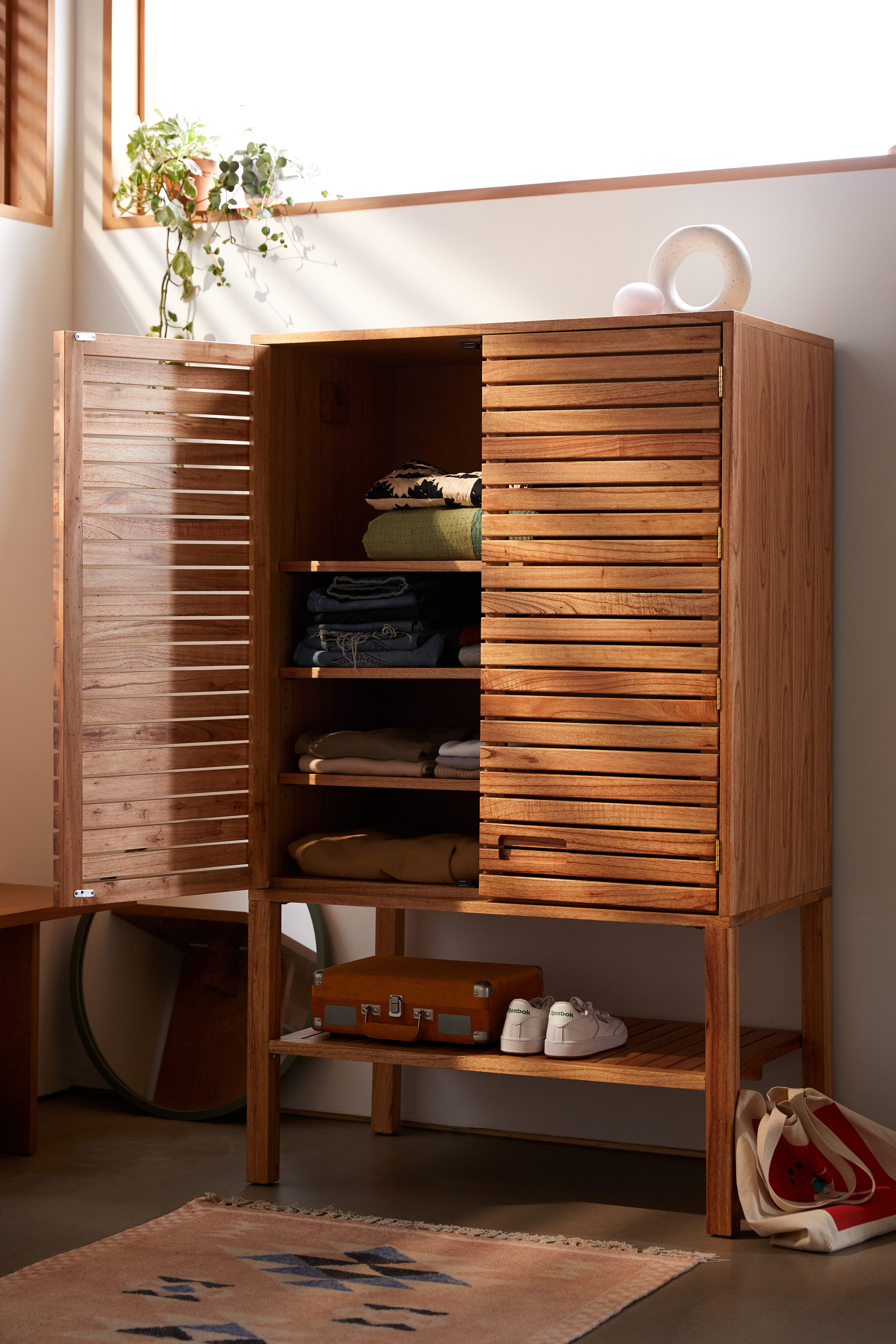 A slatted wood armoire with one door open and shoes on a bottom shelf