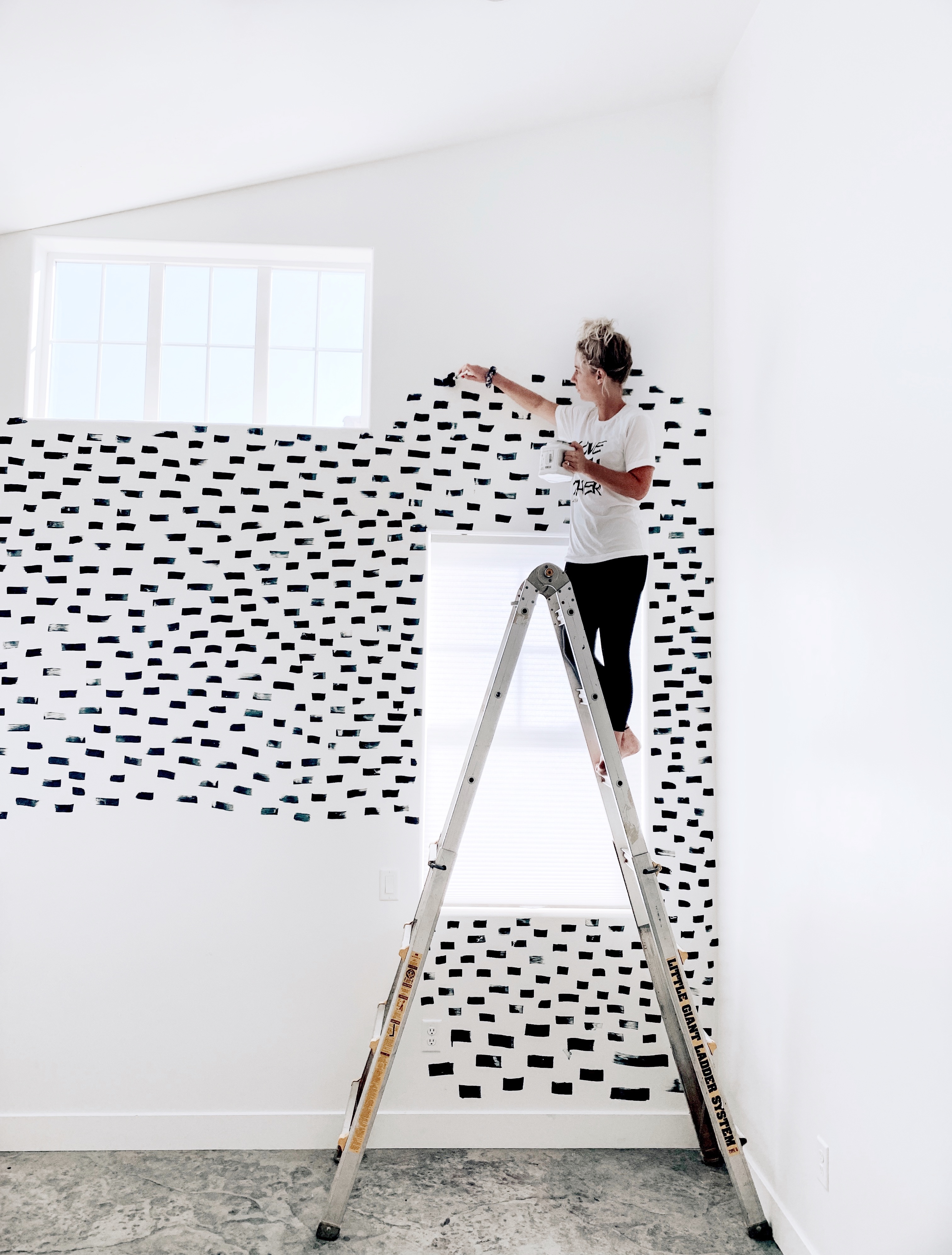 woman on a ladder painting black strokes across the wall