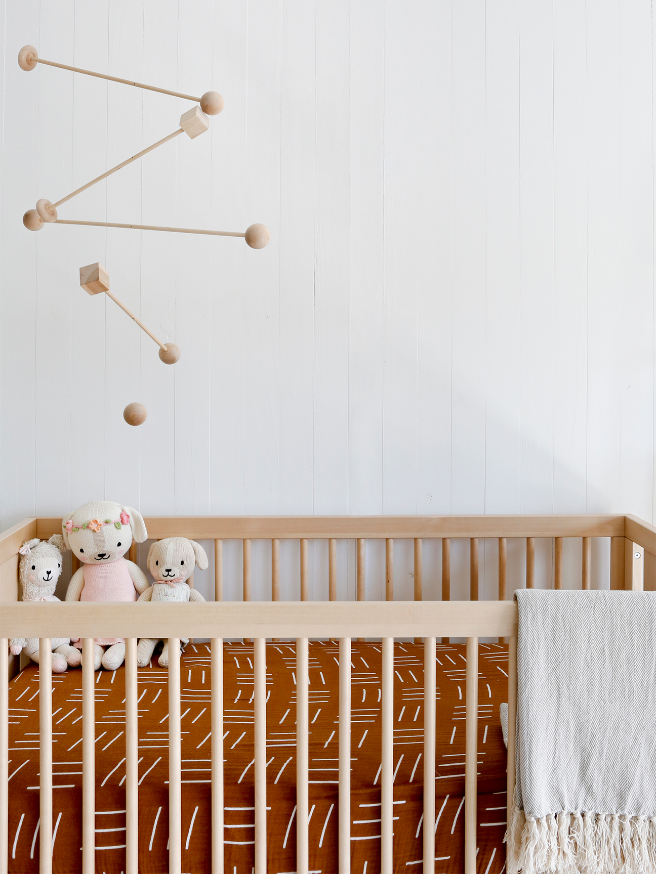 wood mobile hanging over a crib with terracotta colored sheets