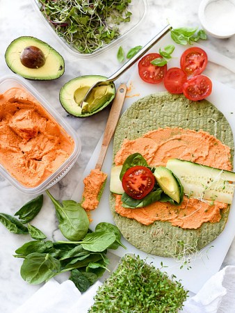 green spinach wrap opened with orange hummus spread