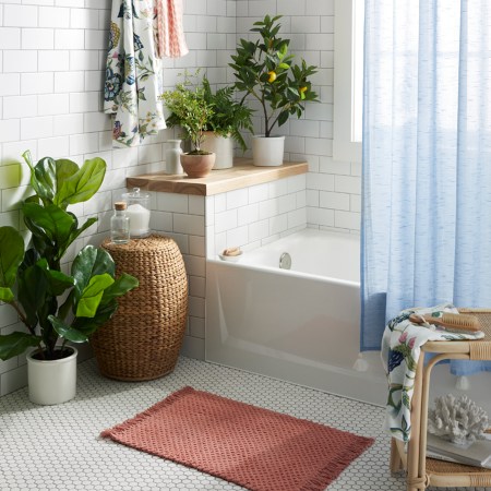 white bathroom with blue shower curtain, plants, and pink bathmat