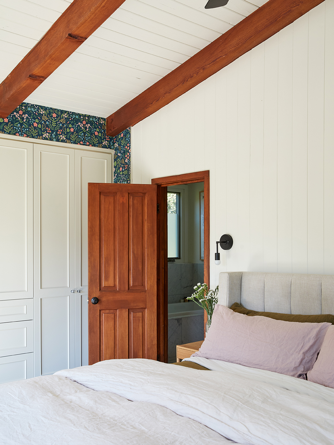 primary bedroom with beige sheets and navy wallpaper.