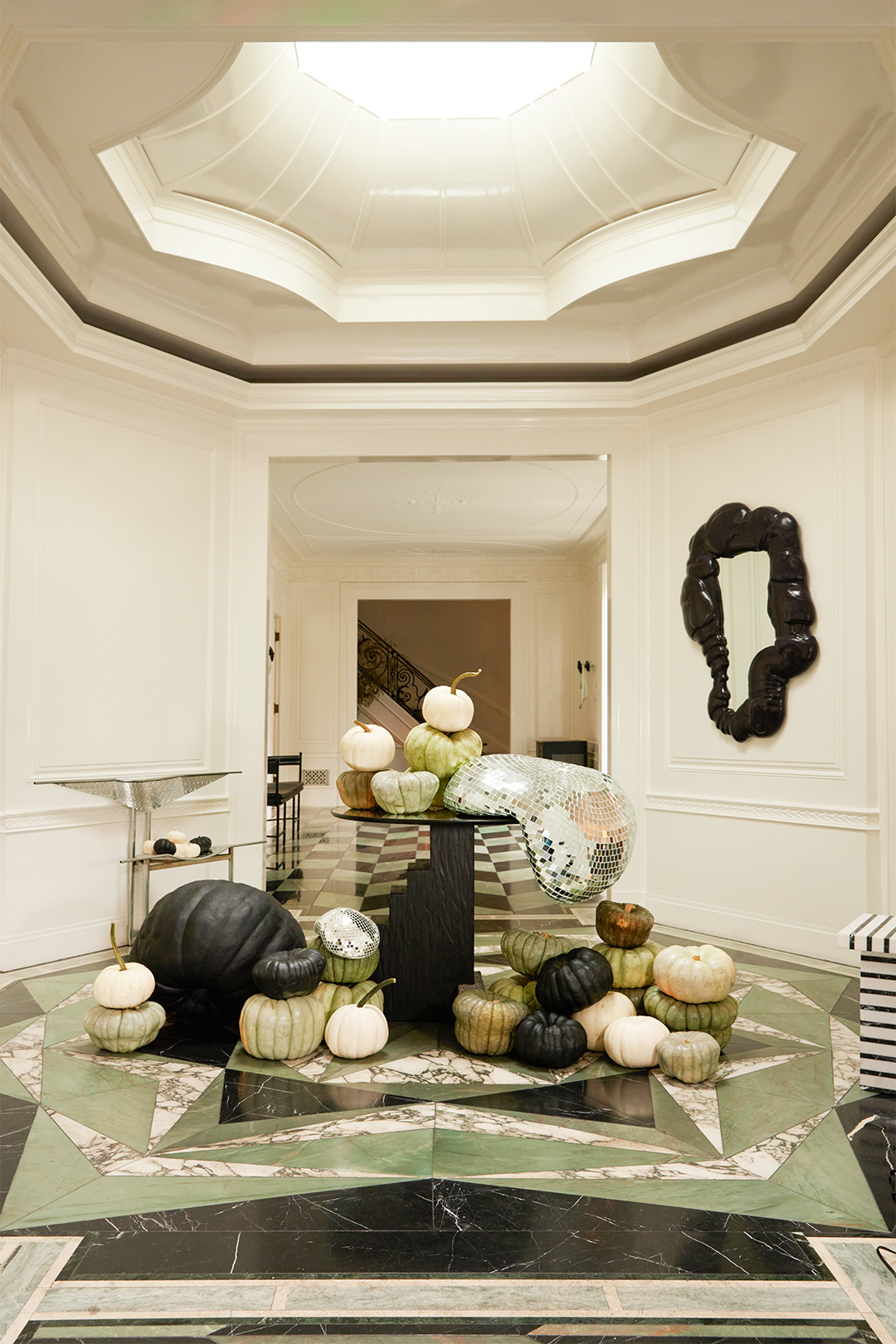 White entryway with painted pumpkins on the MARBLE floor and on tables.