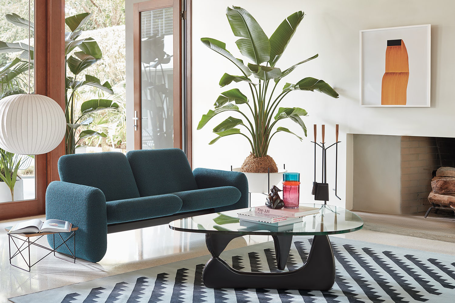 Living room with ink blue sofa, glass coffee table and a plant in one corner