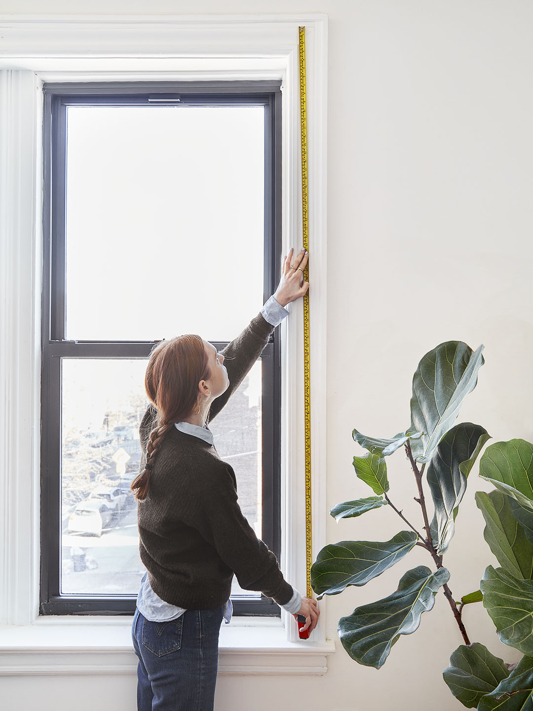 woman measuring window height with yellow tape measure