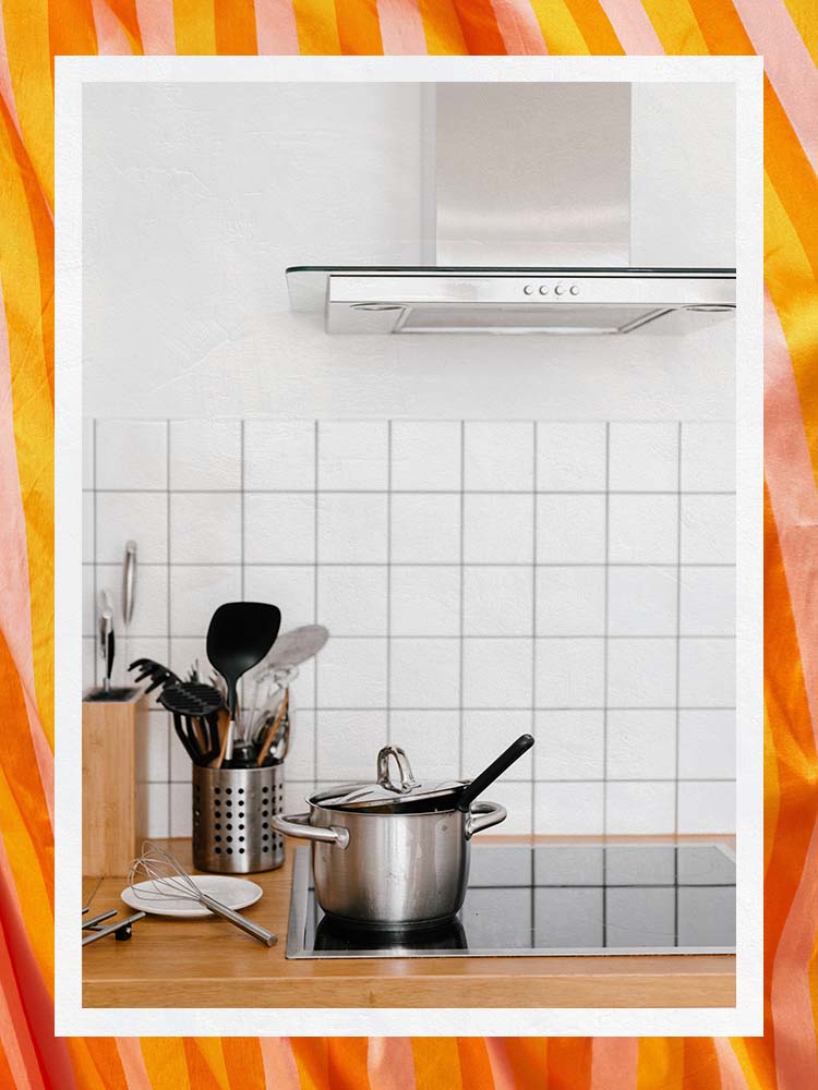 White tile backsplash with small range hood and induction coktop