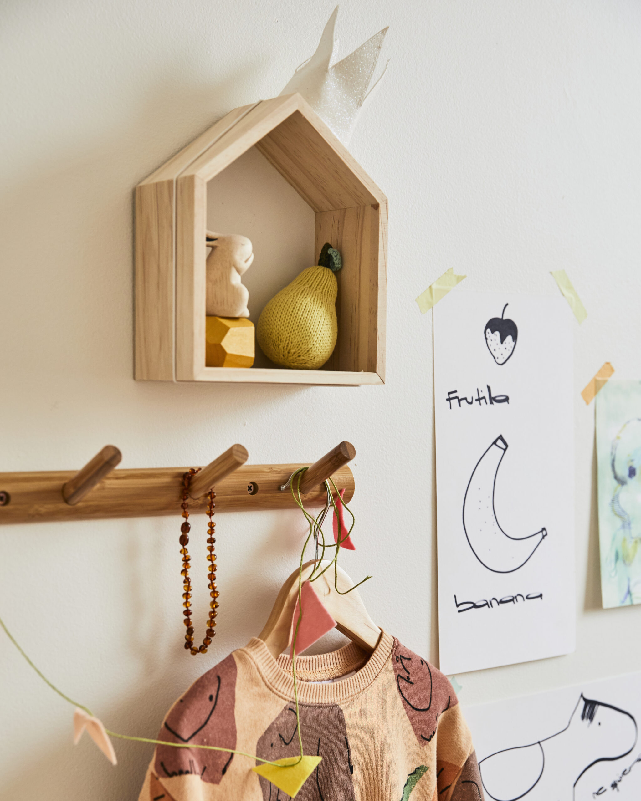 Wood house-shaped shelf above wood peg rail in kid’s room