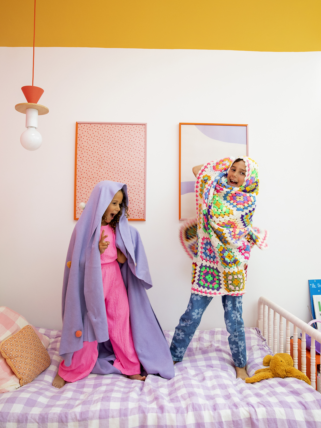 two girls jumping on lavender gingham bed
