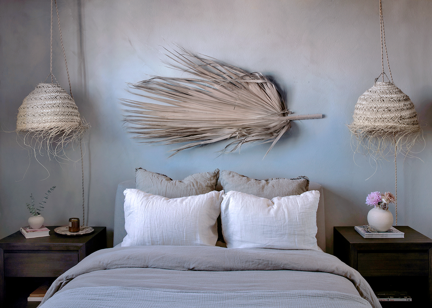 A limewashed bedroom with woven pendant lamps on either side.