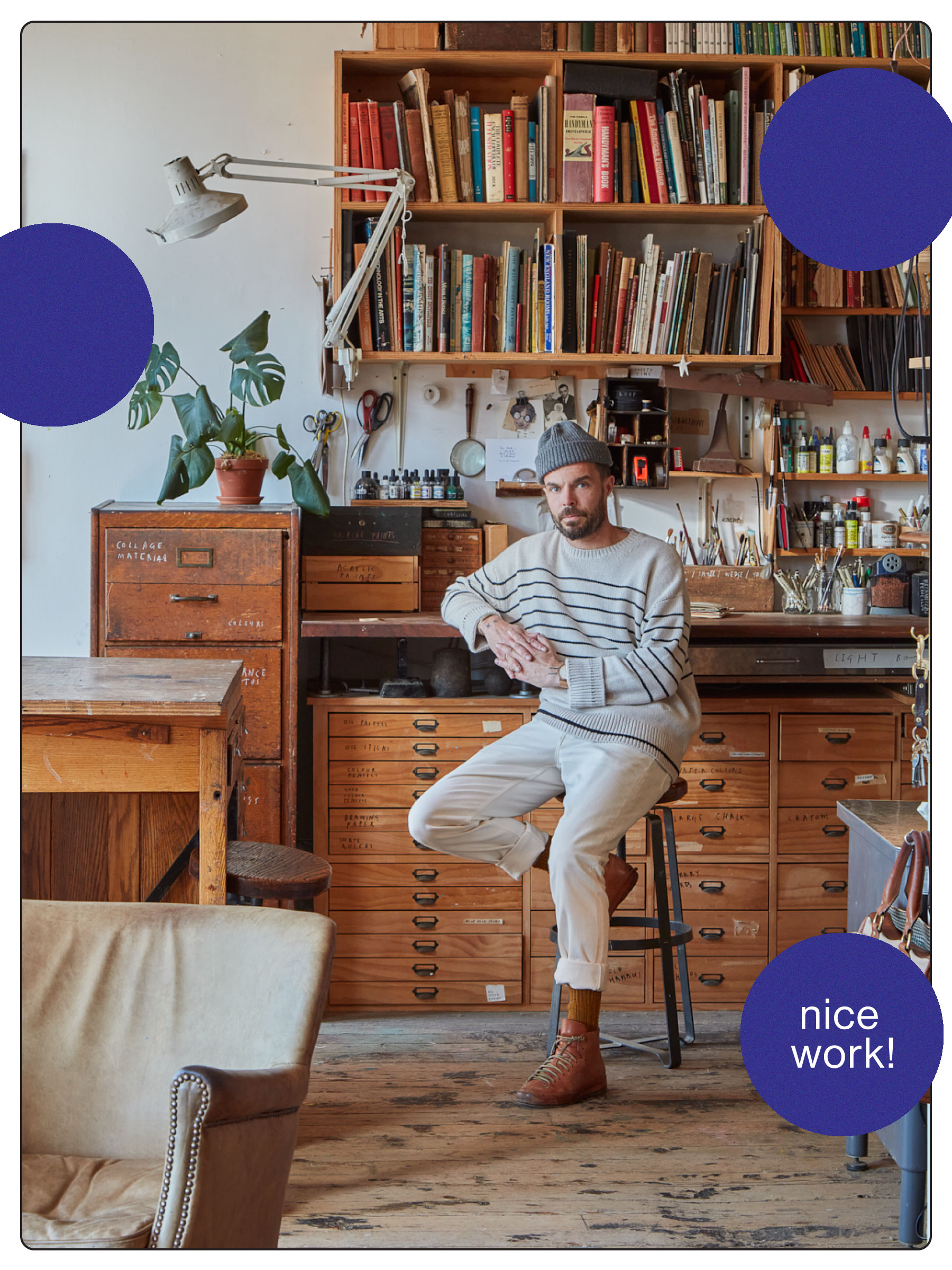 A workshop with a cream armchair on the left in front of wooden shelves and drawers adorned with multicolored books, desk supplies, and two globes. Oliver Jeffers sits on a stool in the center. Three purple polka dots and a white border frame the image. One of the purple dots has "nice work!" written on it in white print.