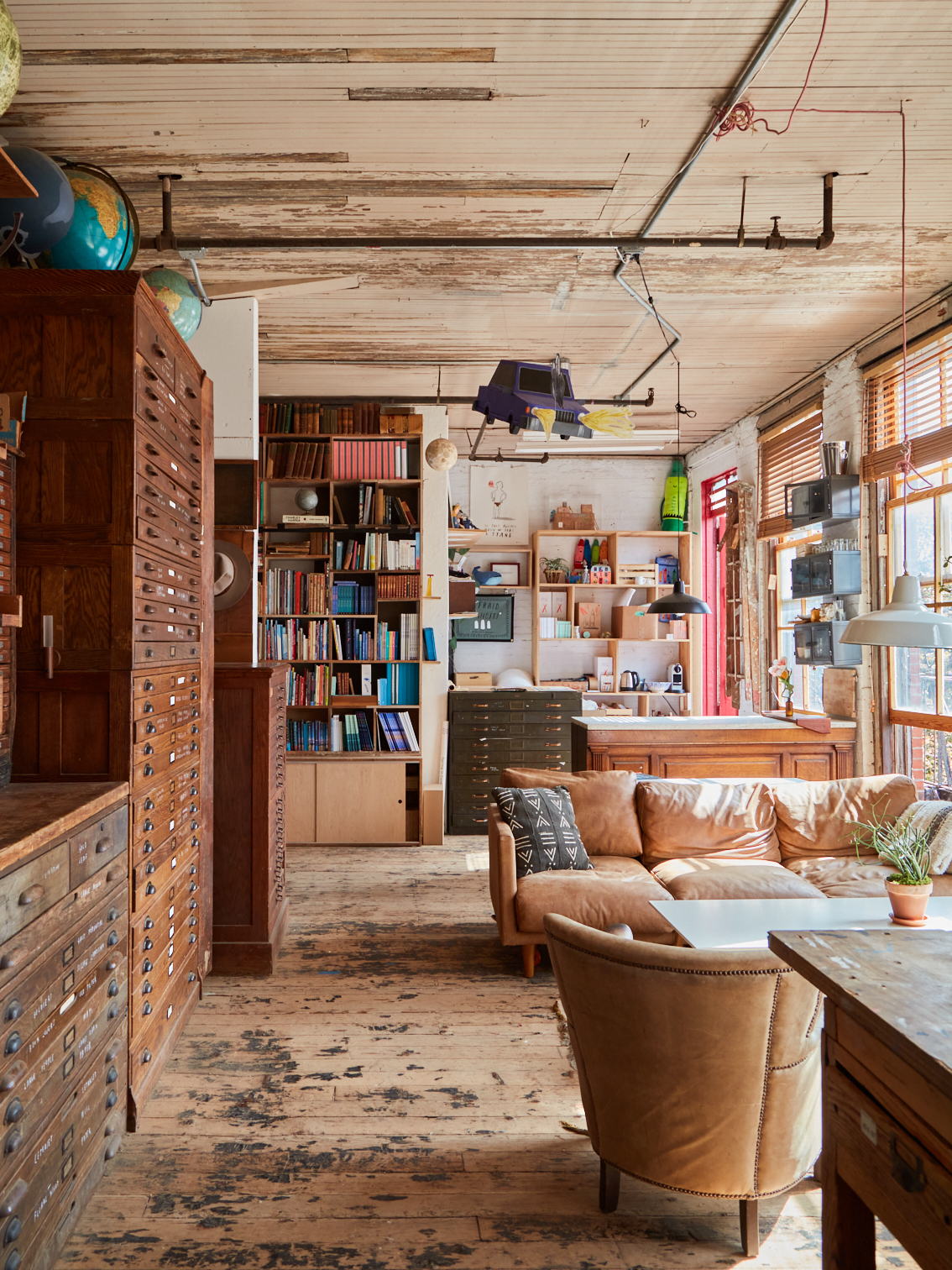 Office space with natural tones seating area to the right and tall wooden drawers on the left. Bookshelves and a desk area are placed towards the back wall.