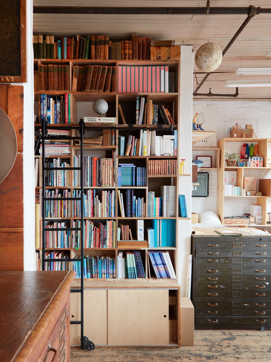 A tall bookshelf and black metal ladder amidst a bright art studio.