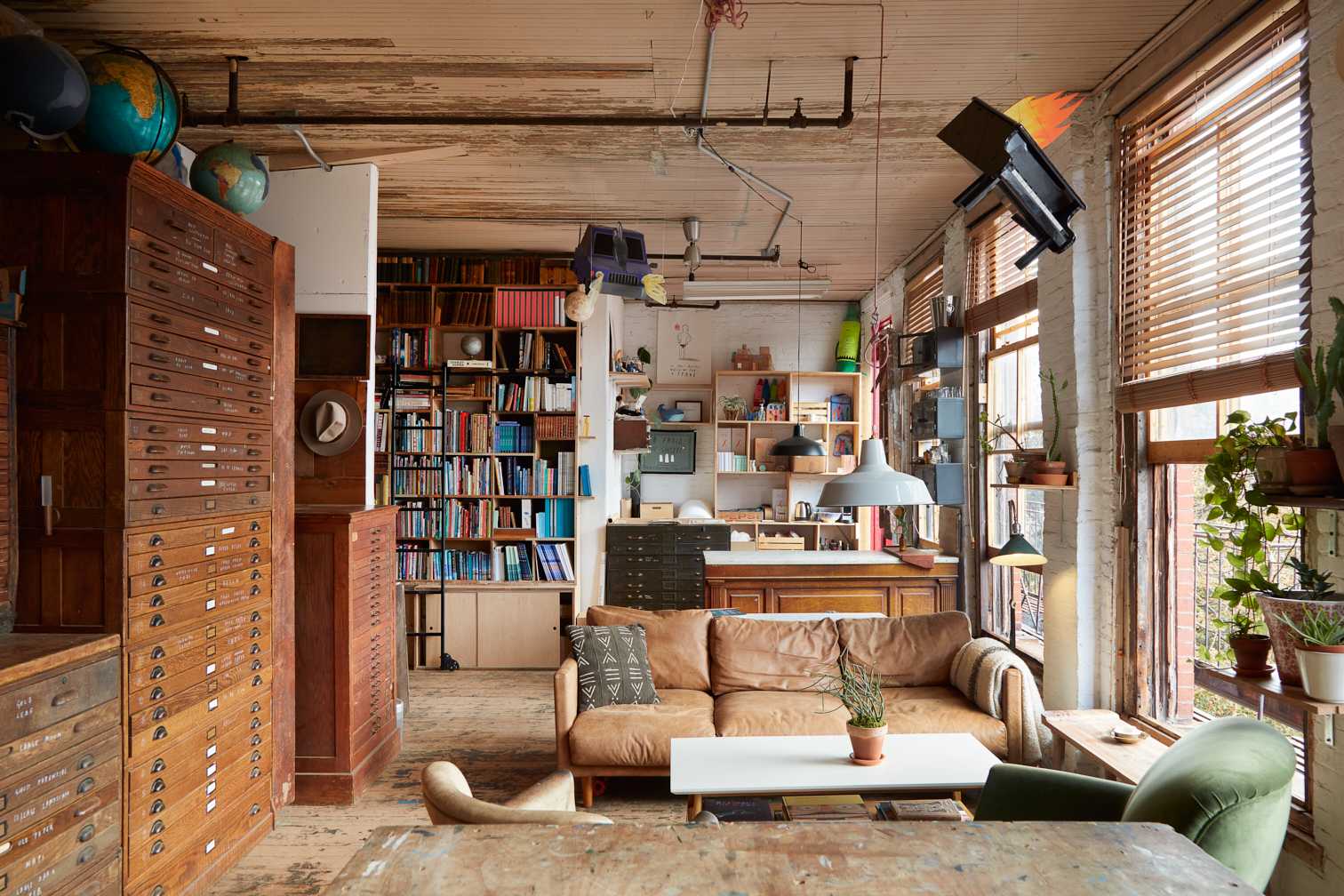 A light brown leather sofa and two armchairs, one green and one white, at the center of an artist's office space.