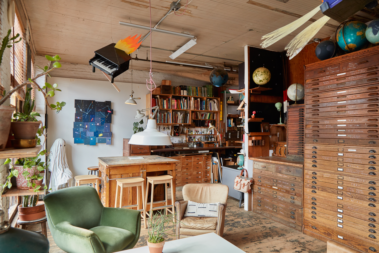 A quirky office space with a seating area towards the front. An a rustic conference table towards the back, with wooden stools around it. Art is hung from the walls and ceiling.