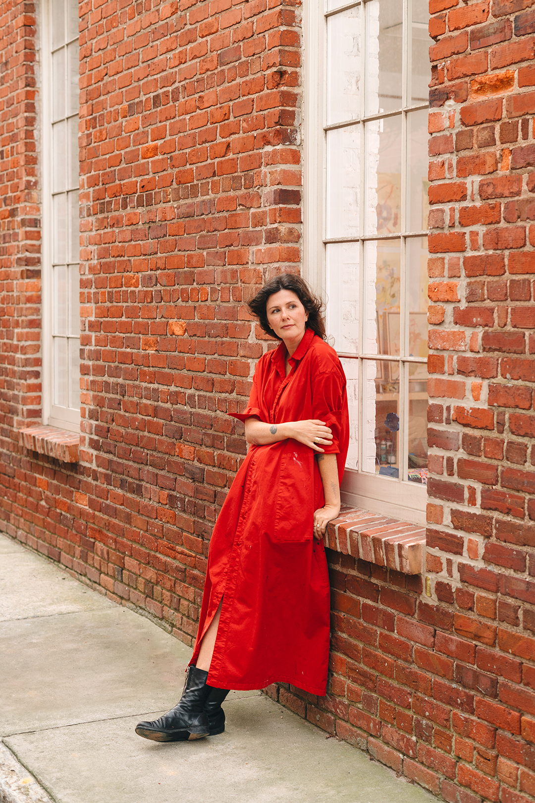 artist in red dress against brick exterior