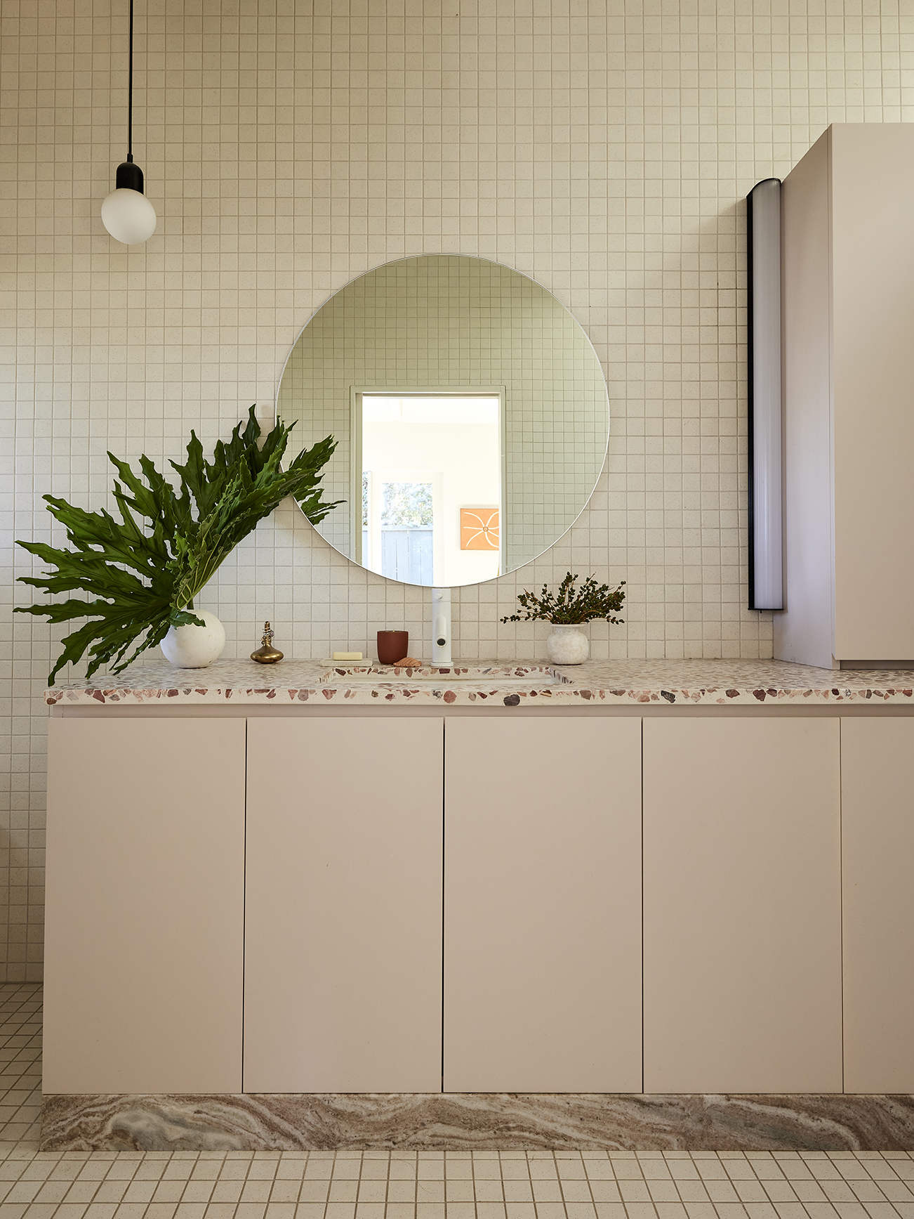 Primary bathroom with round mirror and light pink cabinets