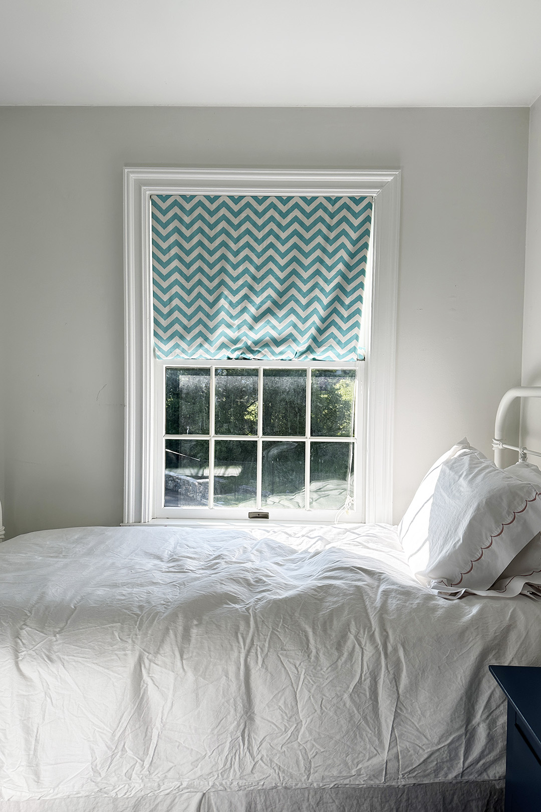 White room with bed and window with turquoise shade.