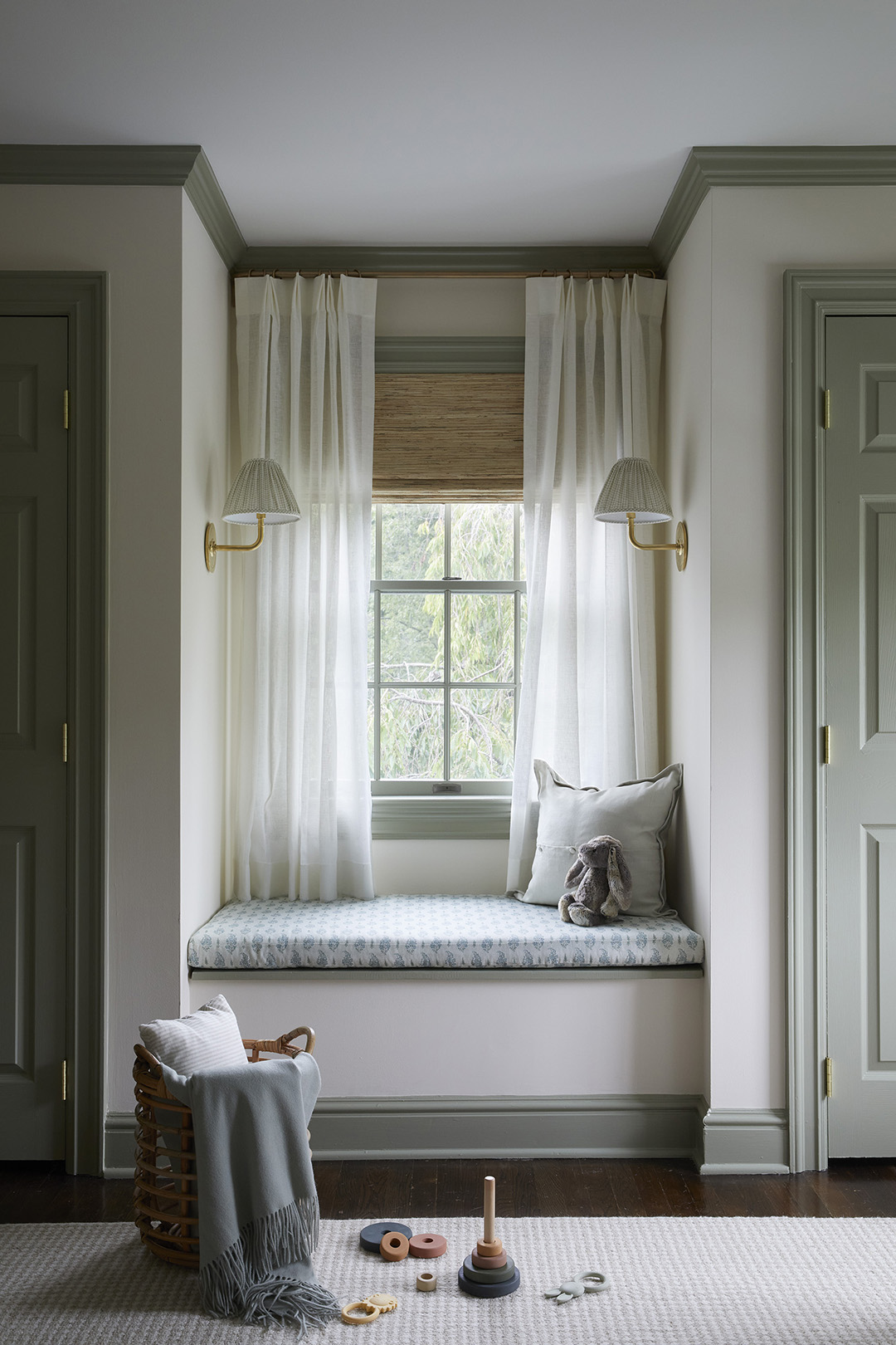 Green and cream room with window seat and baby toys on floor.