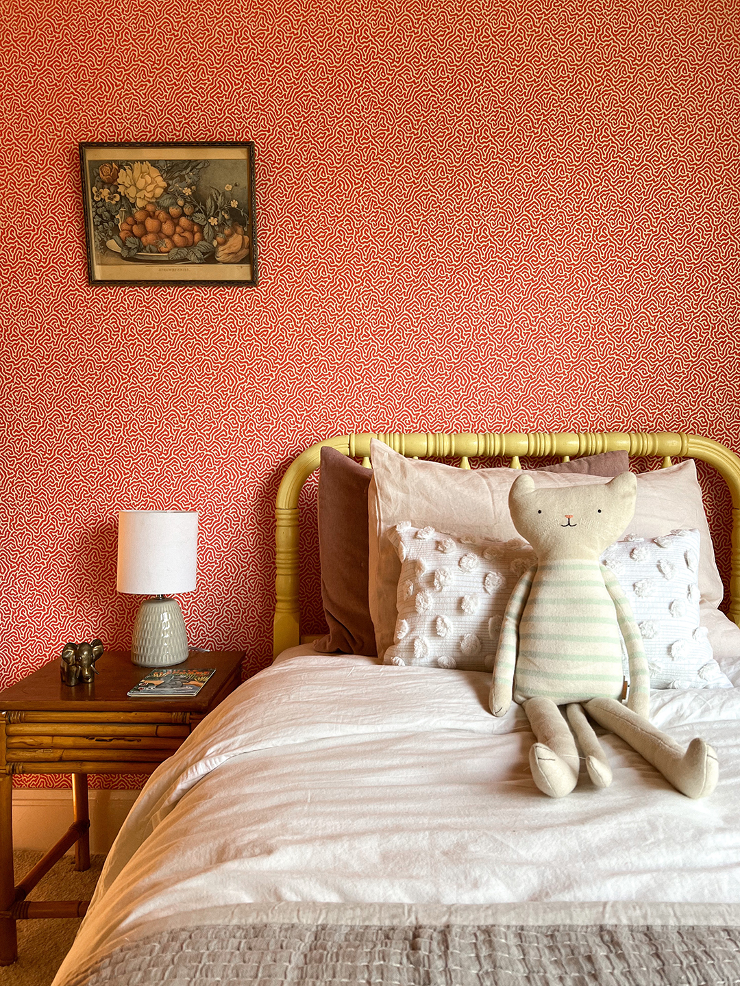 Kid's yellow bed with toy bunny and red wallpaper behind.