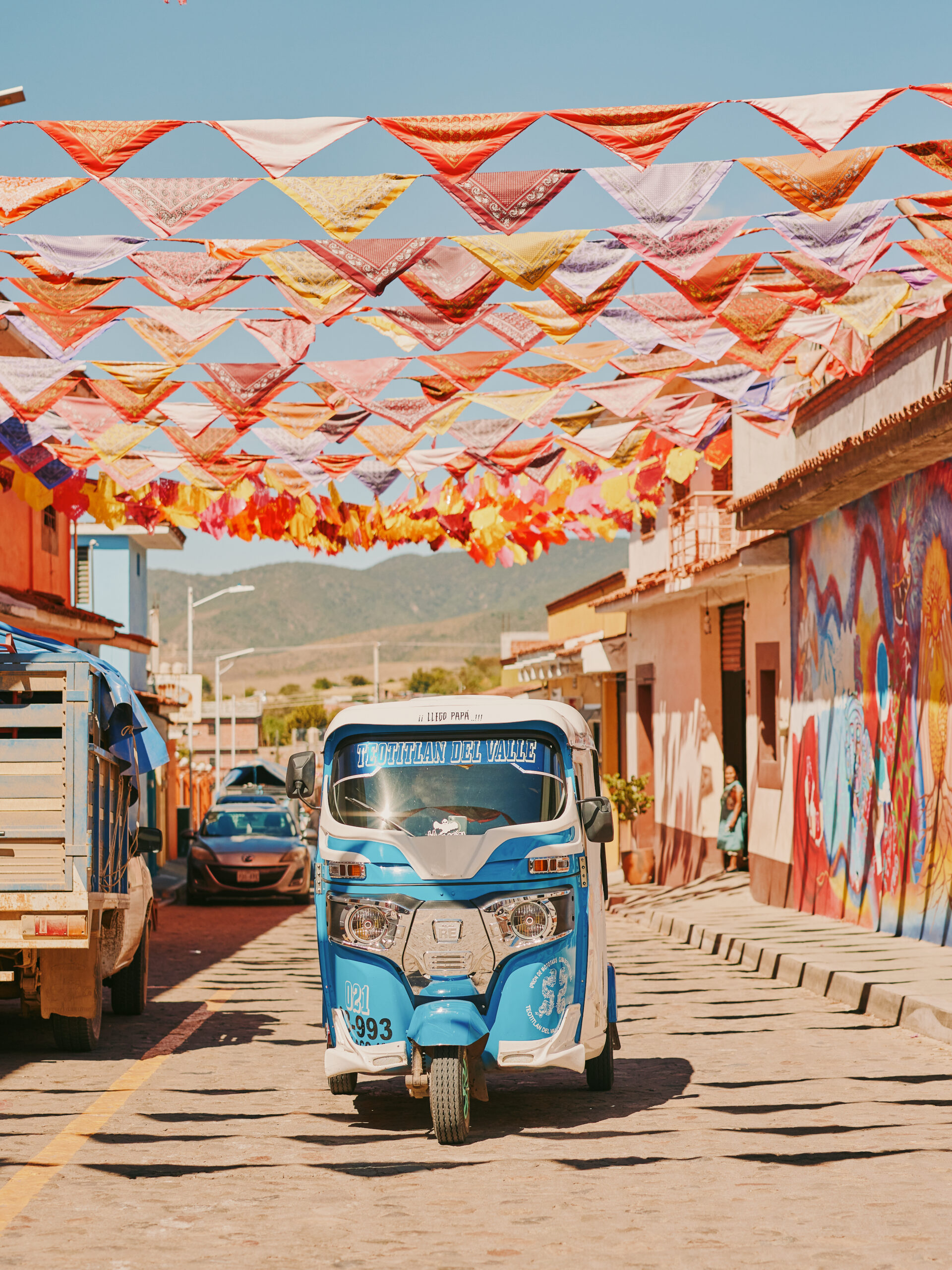 Small blue truck under colorful street flags in Teotitlán del Valle near Oaxaca, Mexico.