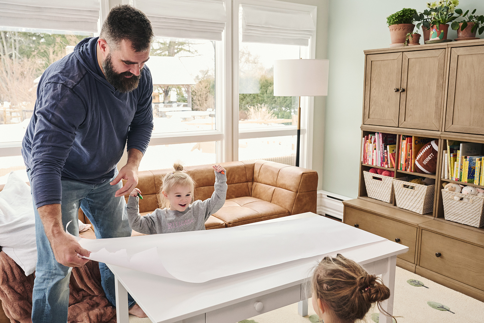 Dad pulling paper across a table for his daughters to draw on