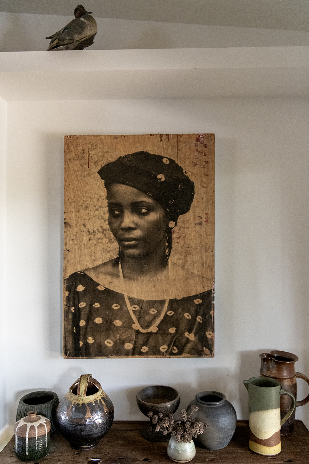 portrait of a woman hanging on a wall in front of pottery