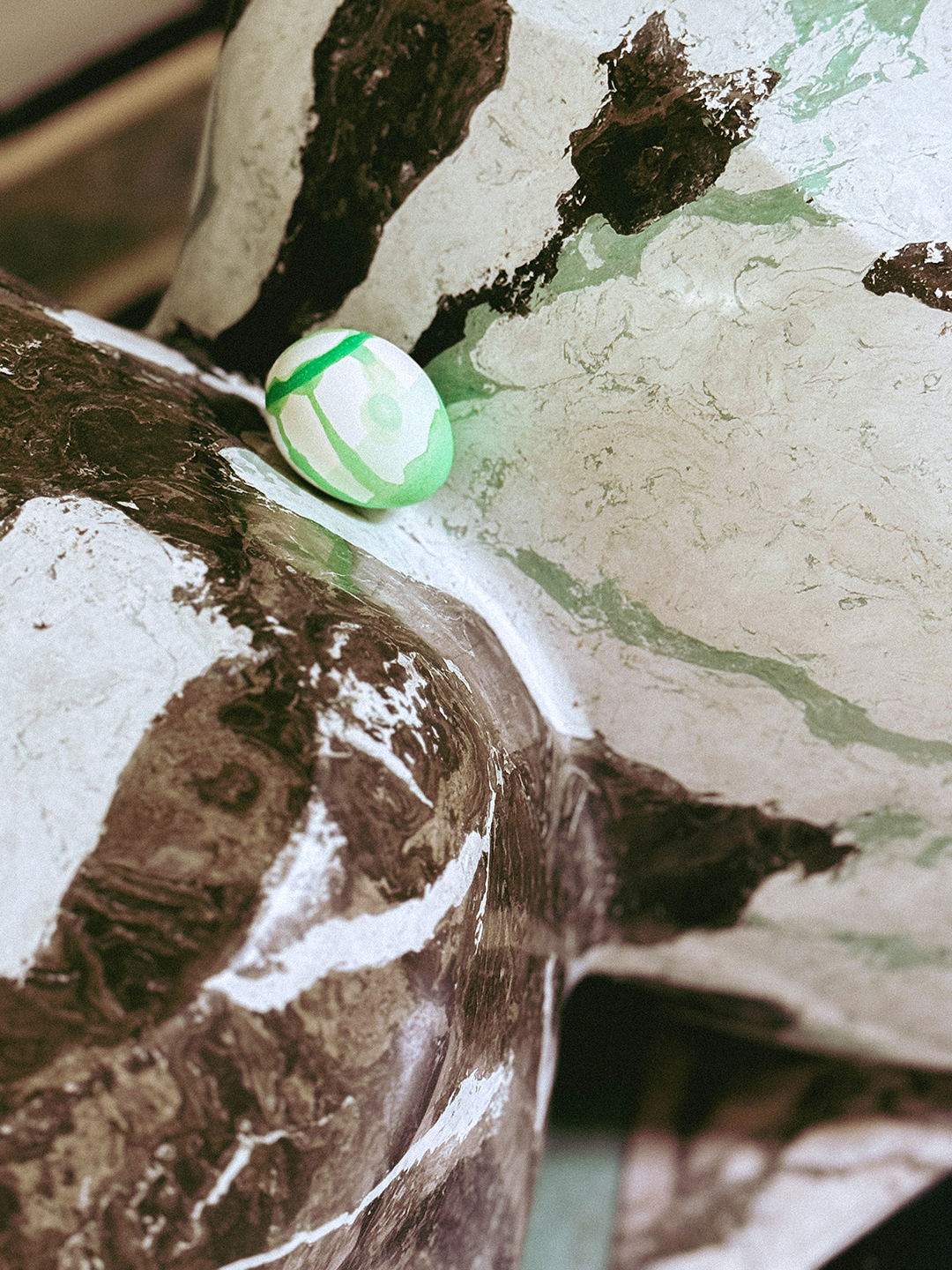 A green drip-dyed Easter egg on a marble surface