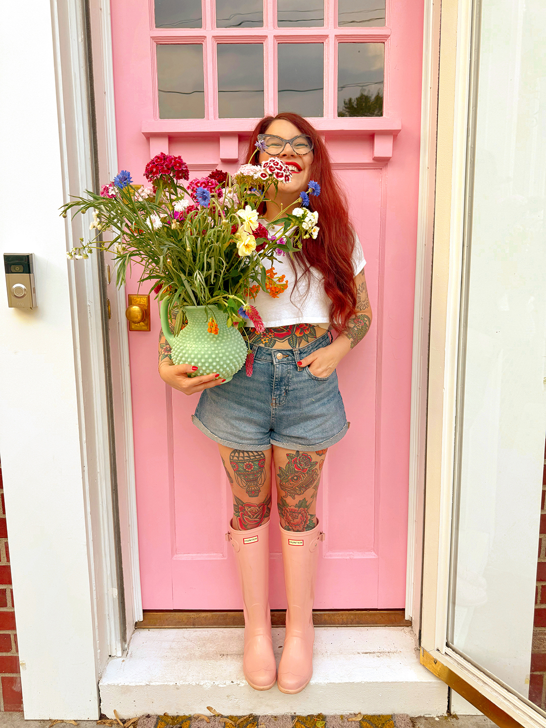 Woman holding vase full of wildflowers in front of pink door